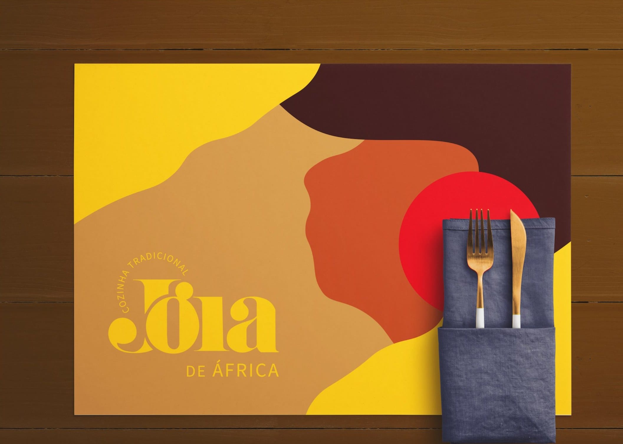 Jóia de África place mat mockup: an illustrated woman's profile in ochre, brown and red with the yellow Jóia logo